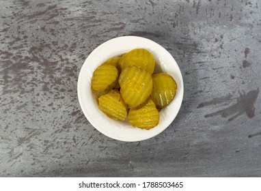 Top View Of A Small White Bowl Filled With Hamburger Dill Pickle Slices On A Gray Tabletop Illuminated With Natural Lighting.