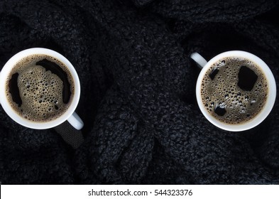 Top view of a small white cups of coffee on a background of black wool scarf with shallow depth of focus