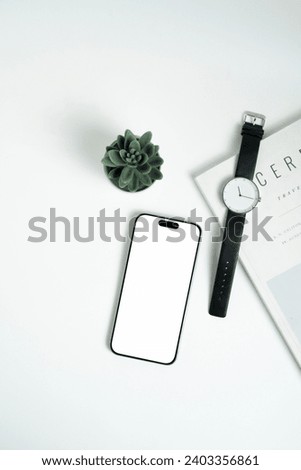 Top view of smartphone with with blank screen, minimalist watches, little plant and magazine on white background. Flatlay