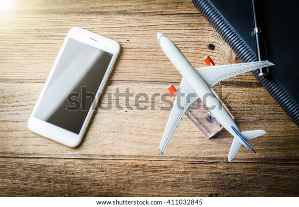 Top view smartphone , book , pen\
and plane on wood plank background. Vintage filter\
effect