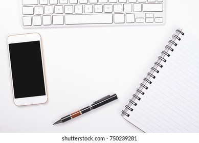 Top view of smartphone and computer keyboard next to notebook and pen on white background. Isolated.