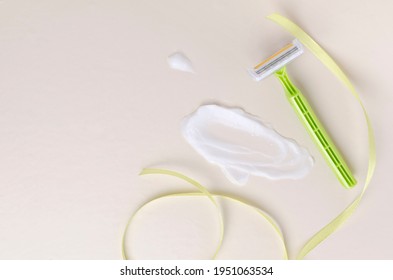 Top View Of Smear Of Hair Removal Cream, Green Razor And Decorative Ribbon On The Ight Beige Surface.Empty Space 