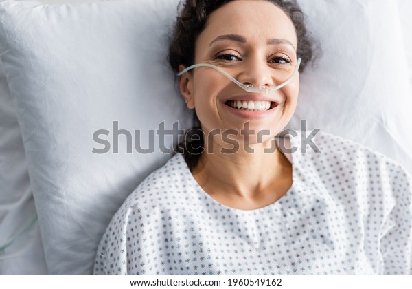top view of smiling african american woman\
with nasal cannula lying in hospital\
bed