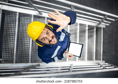 Top View Of Smiling Caucasian Worker Wearing Protective Uniform And Helmet Waving To The Camera In Factory.