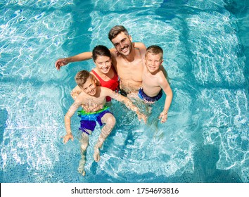 Top view of smiling family of four having fun and relaxing in indoor swimming pool at hotel resort.