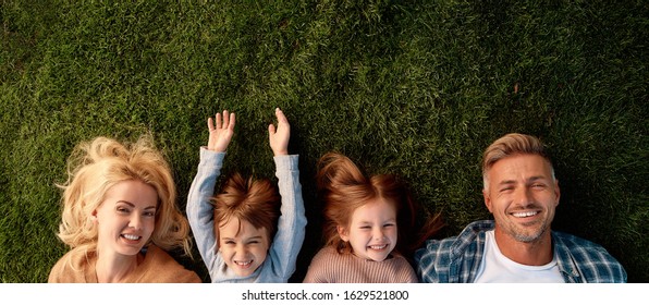 Top view of smiling parents, little girl and boy having fun while lying on a grass. Children, family and nature concept. Horizontal shot