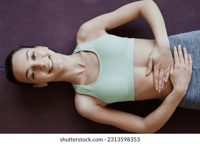 Top view of smiling young woman doing yoga and lying on floor with hands on stomach, copy space - Powered by Shutterstock