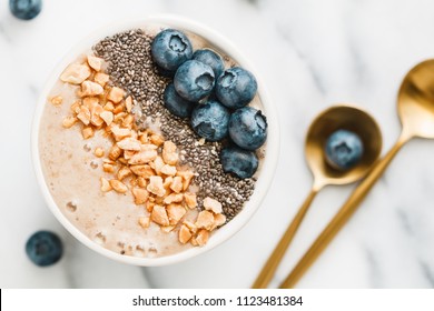 Top View Of A Smoothie Bowl With Fresh Ripe Blueberry, Nuts, Chia, Banana And Soya Milk Over White Background. The Concept Of Healthy Eating And Lifestyle.