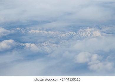 Top view of snow-capped mountains. Snow-covered mountain peaks among the clouds. Beautiful aerial landscape. Great for background. Khabarovsk region, Russia. - Powered by Shutterstock