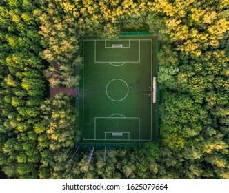 Top View Of A Soccer Field In The Forest, Tall Trees Around The Stadium. Aerial Photography