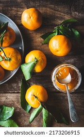 Top view of some tangerines and a glass jar with tangerine jam with a spoon inside, on a rustic wooden table