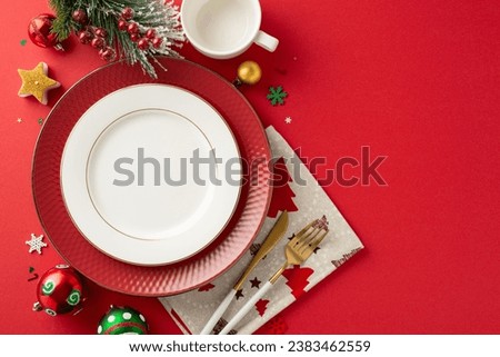 Top view of sophisticated New Year's family dinner table arrangement. Gold cutlery, cup, baubles, candle, and holiday embellishments on red background with open space for text or promotional messages