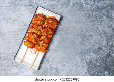Top view So-tteok is a popular South Korean street food consisting of skewered and rice cake bar and sausage topped with white sesame and green onion leaf.