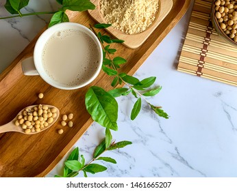 Top view of soymilk cups,soybean seeds on wooden spoon and soy milk powder in a wooden plate background white marble table, is a healthy drink for women because of the "isoflavones" substance