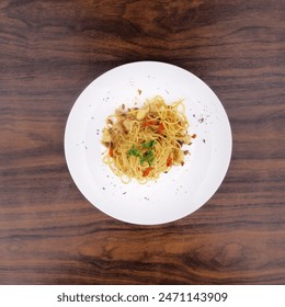 top view of spaghetti aglio e olio, traditional italian pasta with garlic, olive oil and chili peppers in plate on wooden background