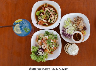 Top view of spicy food  lunch consists of salad flow lotus (root lotus), grilled chicken with Thai spicy sauce, Seafood Glass Noodle Salad served with sticky rice in basket with Blue Hawaiian Soda 