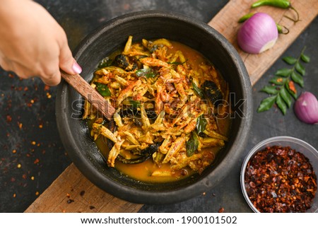 Top view spicy hot anchovy Kerala fish curry. Indian food. Woman hand making Fish curry with red chili, curry leaf, coconut milk. Asian cuisine. Delicious spicy , Bengali , Goan fish curry in clay pot