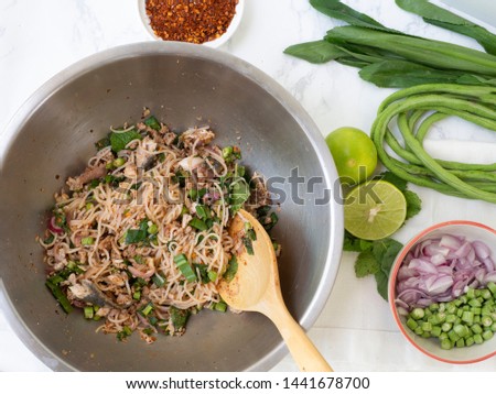 Top view spicy rice noodle with mackerel fish salad in stainless mixing bowl and wood ladle