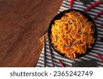 Top view of spicy stir fried instant noodle with white sesame, seaweed sheets, spring onion in black bowl on wooden table background. Asia food