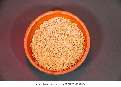 Top view of split yellow moong dal in a clay bowl on a dark background raw organic mung bean lentils, a staple ingredient in indian cuisine, healthy plantbased protein source