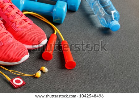 Top view of sports equipment, dumbbells, a skipping rope, a bottle of water, sneakers and a player. Isolated on a gray