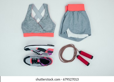 Top view of sportswear with sneakers and skipping rope isolated on grey 
