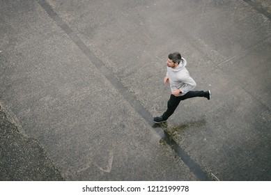 Top View Of Sporty Man Running In Winter On Urban Asphalt. Male Runner Training Outside.