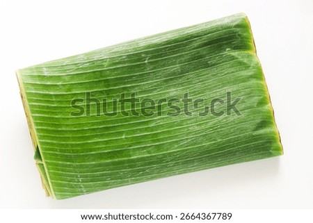 Top view stack of fresh, folded daun pisang (banana leaves) on a white background.