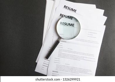 Top view of stack of resume files,magnifier on black surface.Concept of reviewing resume applictaions,searching for new employees - Shutterstock ID 1326299921