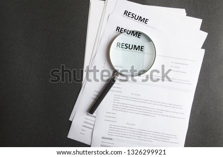 Top view of stack of resume files,magnifier on black surface.Concept of reviewing resume applictaions,searching for new employees