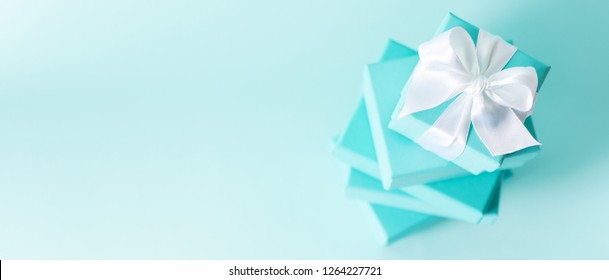 Top View Of Stack Of Tiffany Boxes Tied With Silk Ribbon, Lying On Each Other On Tiffany Blue Color Pastel Background. Gift Festive Selection. Long Wide Banner