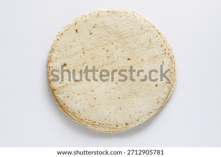 Top view of a stack of tortilla wraps placed on a clean white background, highlighting their soft texture and light, speckled surface.