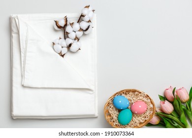 Top view of a stack of white bedsheets sets, cotton branch and a basket with Easter eggs. Copy space.