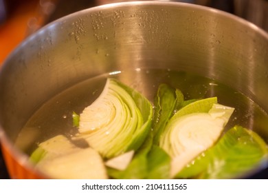 A Top View Of A Stainless Steel Pot Filled With Boiling Water, And Cut Pieces Of Organic Cabbage Cooking On A Restaurant Stove. There's A Turnip In A Food Bag And The Soup Is Being Prepared For A Meal