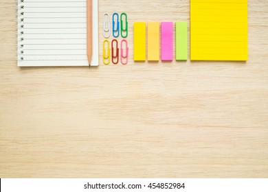 Top View Of Stationery Items - Notepad, Notebook, Sticky Note, Paper Clips, Pencil - On Wooden Background - Desk Above Flat Lay Items On Wooden Table