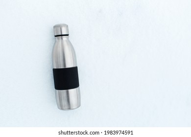 Top View Of Steel Reusable Thermo Water Bottle In Snow. Background With Copy Space.