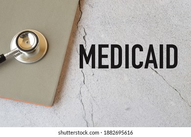 Top View Of Stethoscope And Notebook Over Grey Background Written With MEDICAID.Medicaid In The United States Is A Federal And State Program That Helps With Medical Costs For Some People