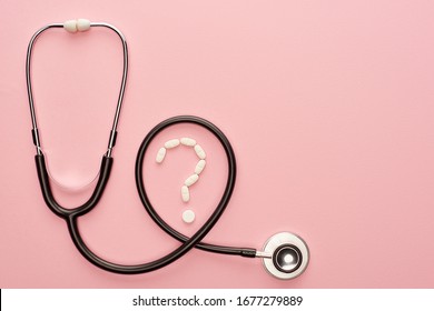 Top view of stethoscope and question mark from pills on pink background