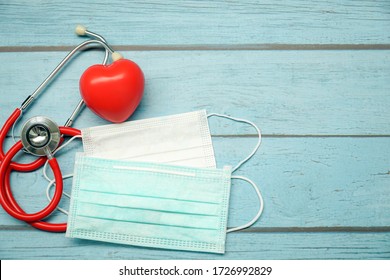 Top View Of Stethoscope, Red Heart And Two Face Mask On Blue Wood Table. Check Up Health During Coronavirus (Covid-19) Epidemic. Wear Mask To Protection Saliva, Cough, Pollution (PM2.5). Copy Space.