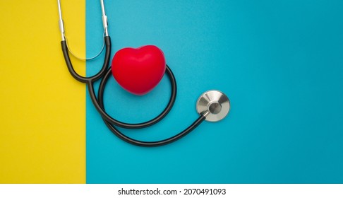 Top view of a stethoscope and a red heart shape on a yellow and blue background. Space for text. Medical and healthcare concept.