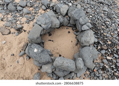 Top view of a stone campfire ring built from large rocks on a sandy beach