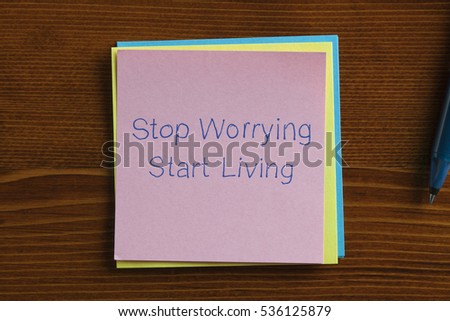 Top view of Stop Worrying Start Living note on the wooden desk with pen aside.