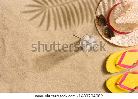 Top view straw hat, sunglasses and glass of water with copy space. Traveler accessories on sand. Travel vacation concept. Summer background. Harsh light with shadows