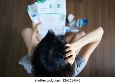 Top view of stressed young Asian woman holding bills and thinking about  finding money to pay credit card debt and all bills. She is holding head by another hand. Financial problem concept.