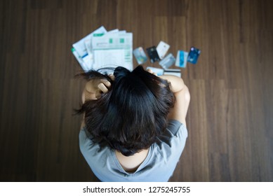 Top view of stressed young Asian woman hands holding the head trying to find money to pay credit card debt and all loan bills. Financial problem from coronavirus or covid-19 outbreak crisis concept.