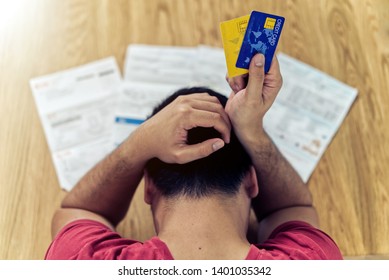 Top View Of Stressed Young Asian Man Holding Credit Cards And Thinking About  Finding Money To Pay Credit Card Debt And All Bills. He Is Holding Head By Another Hand. Financial Problem Concept.