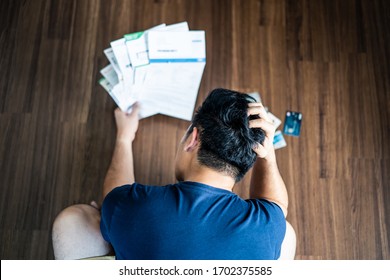 Top view of stressed young Asian man putting hands on head trying to find money to pay credit card debt and all loan bills. Financial problem from coronavirus or covid19 outbreak crisis concept. - Shutterstock ID 1702375585
