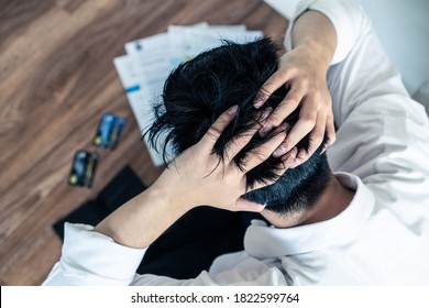 Top View Of Stressed Young Asian Man Sitting And Hugging Knees, Trying To Find Money To Pay Credit Card Debt And All Loan Bills. Financial Problem From Coronavirus Or Covid19 Outbreak Crisis Concept.