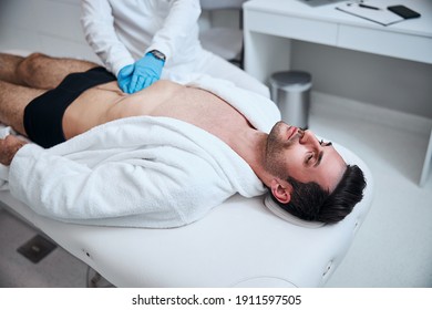 Top view of stubbled guy lying on couch in clinic while physician is examining him with hands