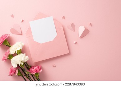 Top view stylish flat lay photo of open envelope with blank card, pretty carnation blooms, and pink paper hearts on a soft pink background